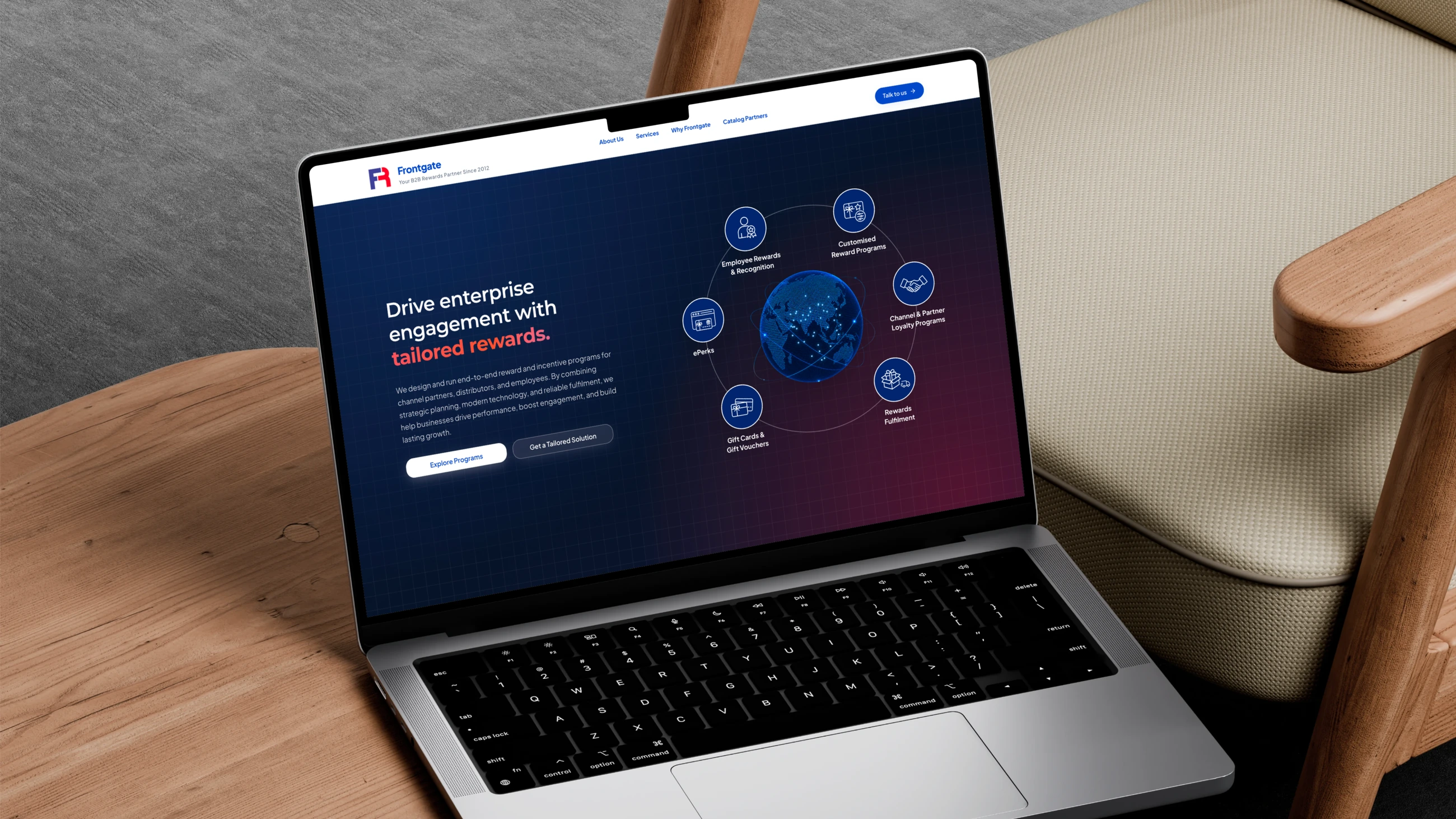 The Frontgate homepage open on a laptop on a wooden side table beside an armchair: &ldquo;Drive enterprise engagement with tailored rewards&rdquo; beside six service icons orbiting a globe